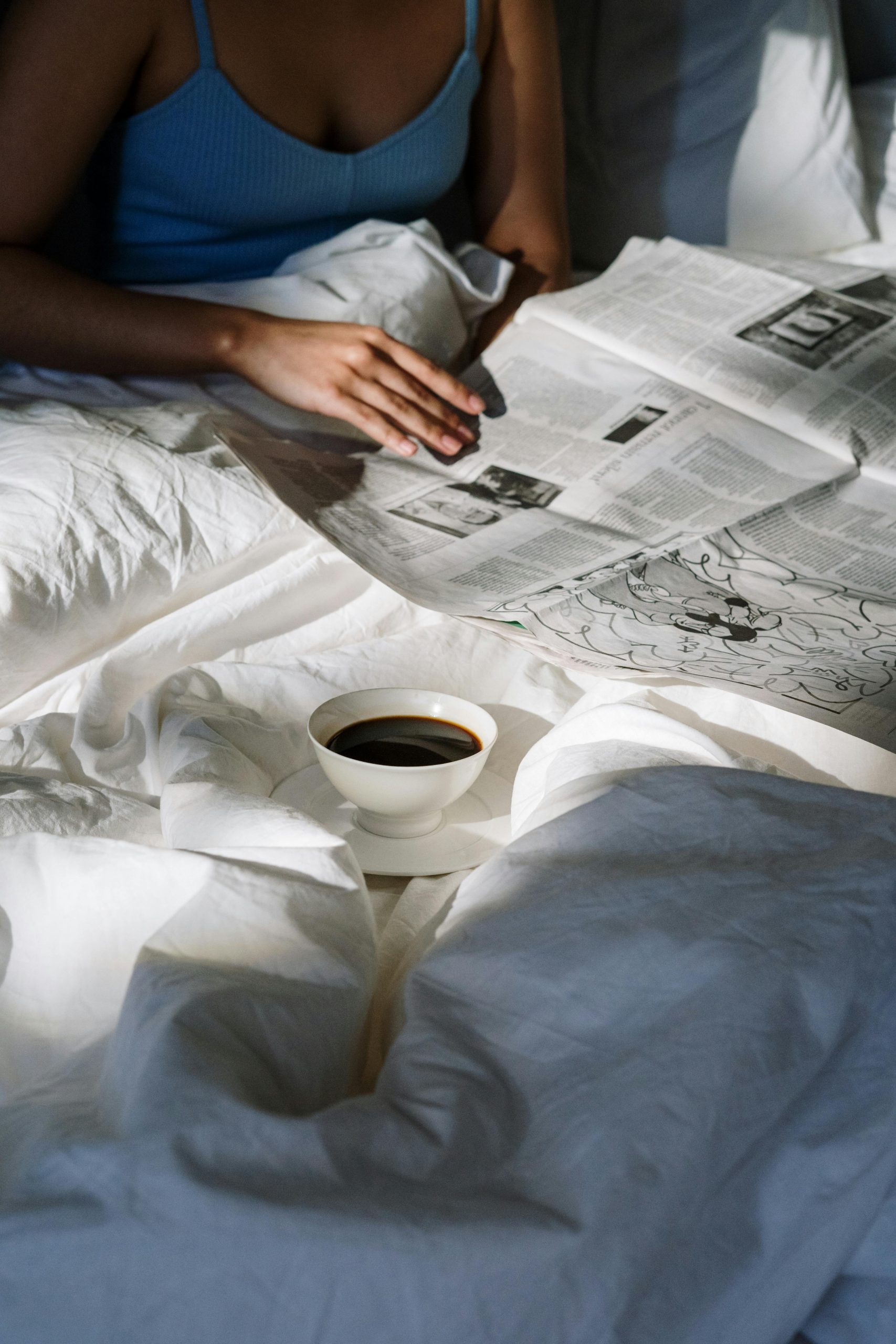 Persoon in bed leest een krant, met een kopje koffie